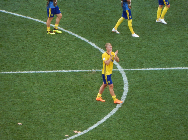Eine Gruppe von Männern in Fußballtrikots und -schuhen auf einem Fußballfeld, mit einer Person in der Mitte, die klatscht.
