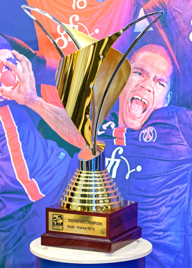 Ein silberner Pokal auf einem Tisch mit einem unscharfen Banner im Hintergrund, das eine Person zeigt.