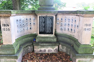Ein Denkmal in einem von Bäumen und einem Zaun umgebenen Park mit einer Tafel an der Wand und trockenen Blättern auf dem Boden, das sich auf dem jüdischen Friedhof in Berlin, Deutschland befindet und als Gedenkstätte für Holocaust-Opfer dient.