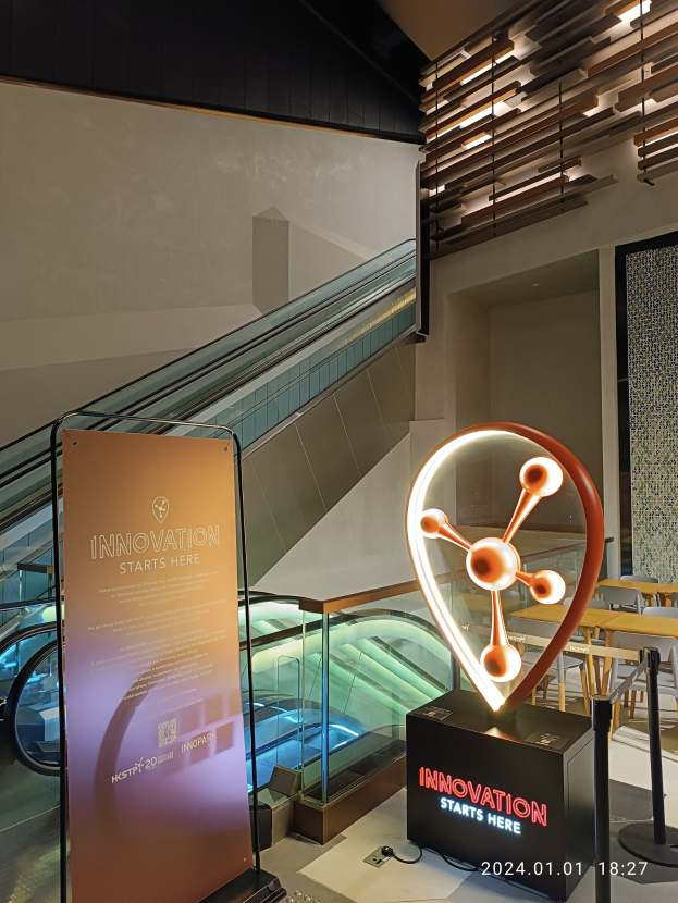 Große Tafel in einem Geböude mit einer Rolltreppe im Hintergrund, Tische und Stühle auf der rechten Seite und eine Tafel mit "Innovation Starts Here" auf der linken Seite, die auf die HSTP20 Expo hinweist.