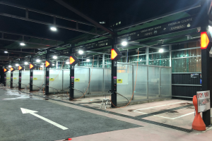 Ein Parkplatz voller Autos unter Deckenlampen, mit Pfählen, Texttafeln und verstreuten Gegenständen auf dem Boden und einer Glaswand im Hintergrund, was auf eine Autowäsche in Seoul, Südkorea, hinweist.