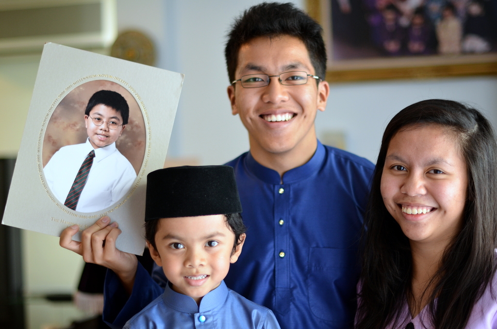 Ein Paar und ein Junge lächeln, wobei der Mann ein Fotoalbum hält und im Hintergrund ein Fotoalbum an der Wand zu sehen ist.