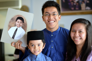 Ein Paar und ein Junge lächeln, wobei der Mann ein Fotoalbum hält und im Hintergrund ein Fotoalbum an der Wand zu sehen ist.