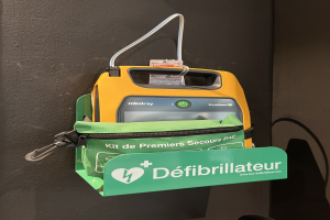 Ein gelb-grüner Defibrillator auf einem schwarzen Tisch mit einer grünen markierten Tasche daneben.