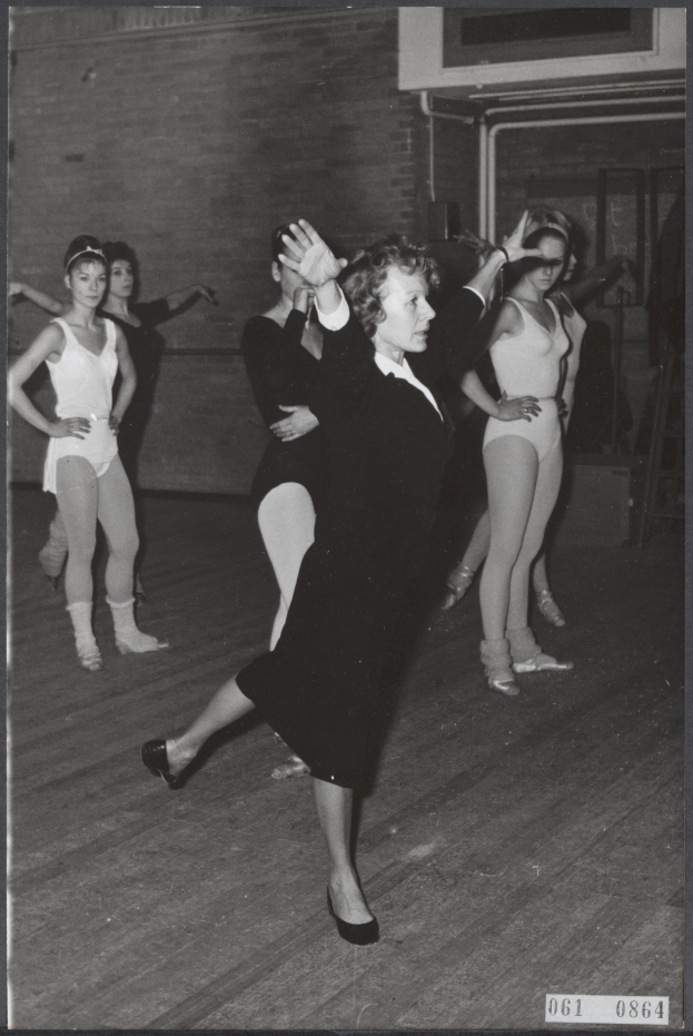 Eine Gruppe von Frauen tanzt in einem Schwarz-Weiß-Foto, wobei die Frau in der Mitte Tanzschuhe trägt, in einem Tanzstudio mit einer Wand im Hintergrund.