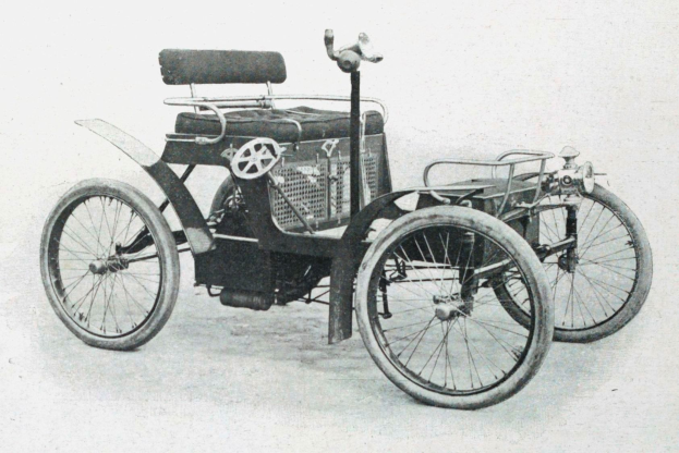 Vintage-Foto in Schwarz-Weiß von einem frühen elektrischen Auto aus den 1900er-Jahren mit schlankem, aerodynamischem Design, großem runden Scheinwerfer, gewölbter Dachlinie, vier großen Rädern, prominentem Heckmotor, hellbeigem Polster und Armaturenbrett mit Knöpfen und Hebeln.