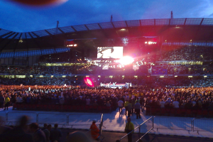 Ein Konzertsaal mit Menschen, Bühnenlicht und einem Projektionsschirm.