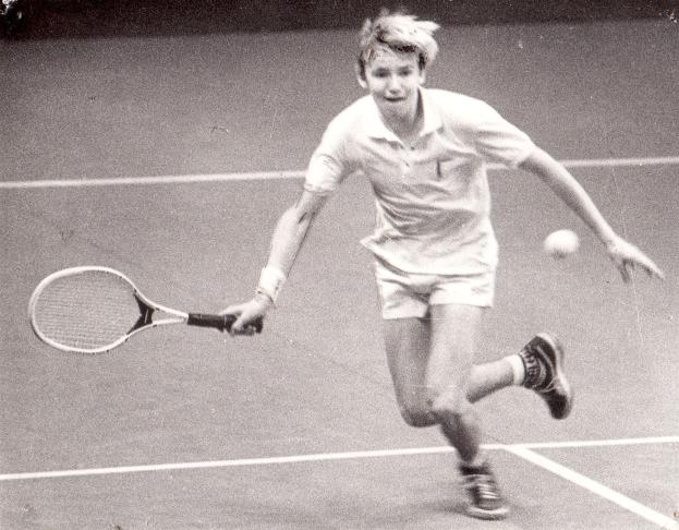 Ein junger Mann in weißer Tennisbekleidung hält einen Schläger und bereitet sich auf den Schlag vor.