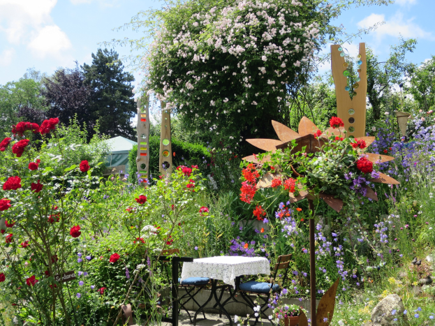 Ein farbenfroher Garten auf dem Chelsea Flower Show mit bunten Blumen und Pflanzen, einem Tisch mit einer Decke umgeben von Stühlen und Bäumen unter einem bewölkten Himmel.