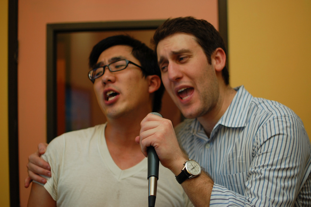 Zwei Personen, die Mikrofone halten und singen, wobei die Person rechts eine Uhr trägt.