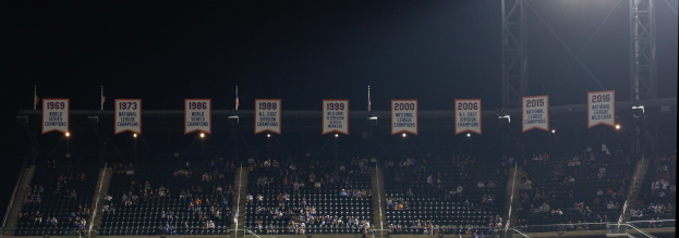 Ein hell erleuchtetes Baseball-Stadion mit Zuschauern auf den Rängen, umgeben von beleuchteten Bannern, vor einem dunklen Hintergrund.