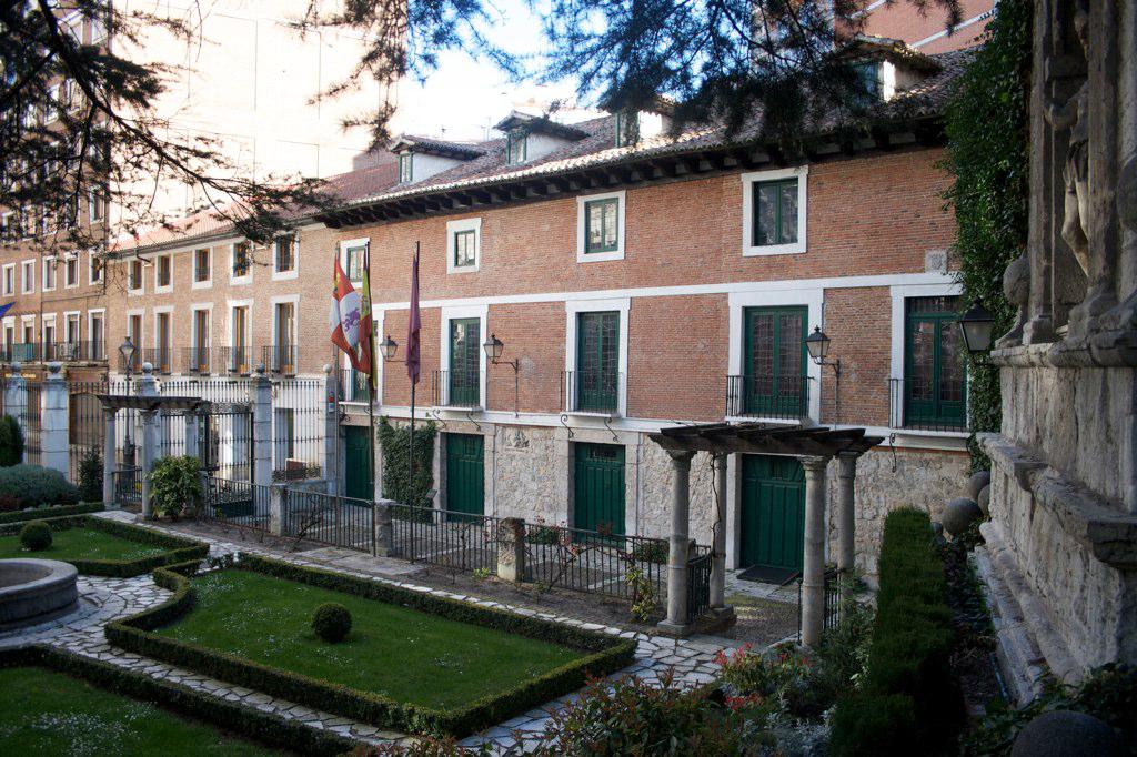 Mehrere Gebäude mit Flaggen, Grünflächen, Pflanzen und einer Zaunwand in der rechten Ecke.