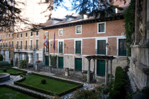 Mehrere Gebäude mit Flaggen, Grünflächen, Pflanzen und einer Zaunwand in der rechten Ecke.