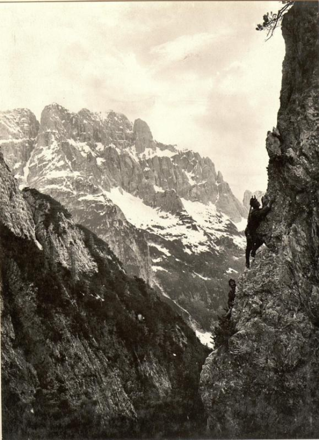 Ein Schwarz-Weiß-Foto eines Mannes, der einen schneebedeckten Berg erklimmt, mit dem Text "Gustav Klimt - Die Drei Gipfel" unten.