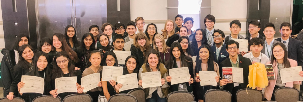 Gruppe von Menschen mit Urkunden in einem Raum mit Stühlen und einer Wand im Hintergrund, wahrscheinlich feiern sie eine Abschlussfeier für das akademische Jahr 2019-2020.