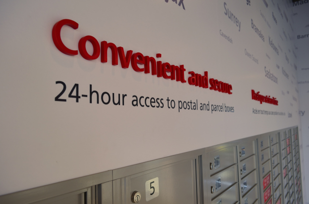 Wandtafel mit Werbung für 24-Stunden-Zugang zu Post- und Paketfächern, mit nummerierten Fächern darunter.