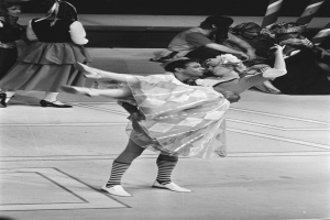 Ein Schwarz-Weiß-Foto eines Paares, das auf einer Bühne tanzt, mit ein paar Menschen auf der Treppe im Hintergrund und einem Pfosten im Vordergrund.