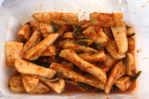 Ein Plastikbehälter voller goldbraun frittierter Tofu und bunter Gemüse, darunter grün, gelb und rot, auf einem Tisch.