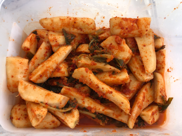 Ein Plastikbehälter voller goldbraun frittierter Tofu und bunter Gemüse, darunter grün, gelb und rot, auf einem Tisch.