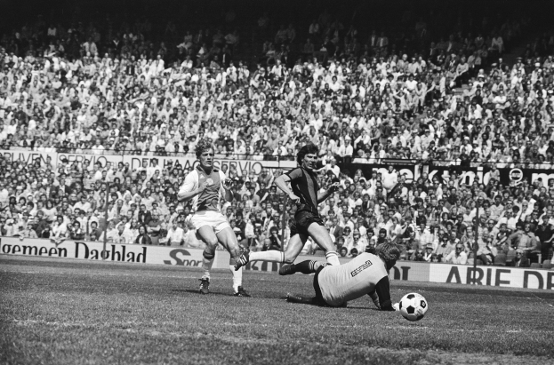 Schwarzes und weißes Foto von Männern, die auf einem Feld Fußball spielen, mit Zuschauern im Hintergrund und einer Bundesliga 1978-79 Ajax 1-1 Hannover 96-Banner.