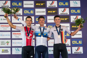 Drei Männer stehen auf einem Podium, jeder trägt eine Medaille und hält einen Blumenstrauß, im Hintergrund ist ein 'Giro d'Italia'-Schild zu sehen.