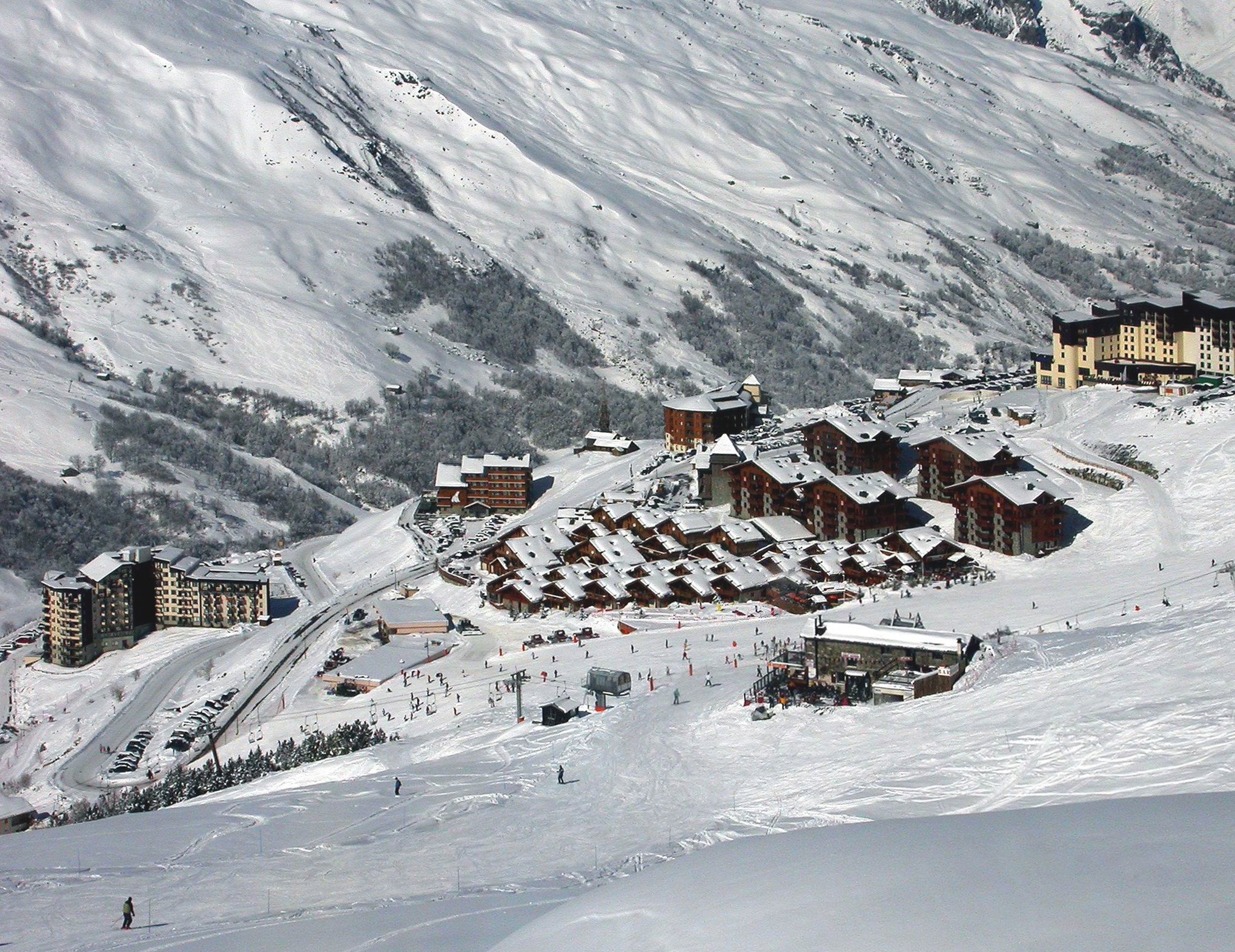 Ein malerischer Blick auf ein Skigebiet in den französischen Alpen, mit schneebedeckten Bergen, Gebäuden, Bäumen und Skifahrern auf den Pisten.