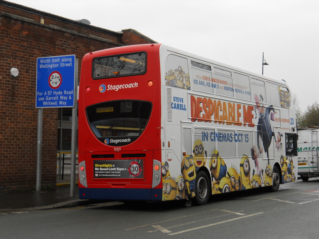 Ein weißer und roter Bus parkt auf einer Straße mit einer roten Backsteinmauer und einem blauen Warnschild im Hintergrund.