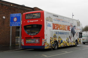 Ein weißer und roter Bus parkt auf einer Straße mit einer roten Backsteinmauer und einem blauen Warnschild im Hintergrund.