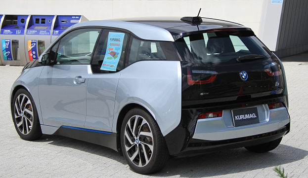 Ein BMW i3 Elektroauto vor einem Gebäude geparkt, mit einer Pflanze im Vordergrund und einer Wand im Hintergrund, das ein zentral positioniertes Rad zeigt.