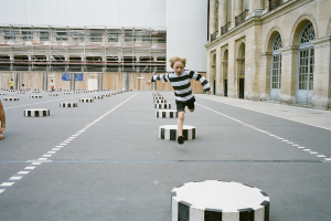 Vier Kinder befinden sich in einem Schulspielplatz mit schwarzen und weißen Zementstufen, ein Kind läuft auf dem Boden.