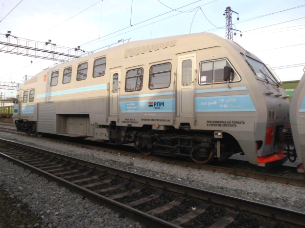 Eine diesel-elektrische Lokomotive fährt auf Schienen neben einem anderen Zug, mit Strommasten und Kabeln im Hintergrund unter einem klaren blauen Himmel.