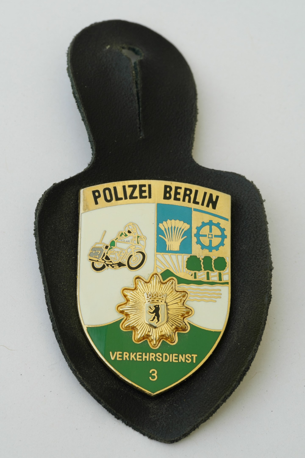 Ein schildförmiges Polizeibadged mit "Polizei Berlin" in fetter schwarzer Schrift auf einem blauen Hintergrund, das ein weißes Stern in der Mitte und einen weißen Rand hat.