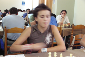 Ein Raum mit Menschen an Tischen beim Schachspielen, eine Vorhangwand mit einem Foto in der Ecke.