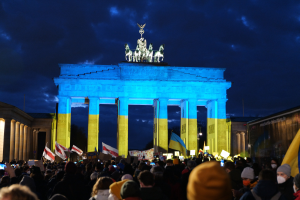 Eine Menschenmenge steht vor dem Brandenburger Tor in Berlin, Deutschland, mit Fahnen und Schildern, mit einer Fahne auf der rechten Seite.