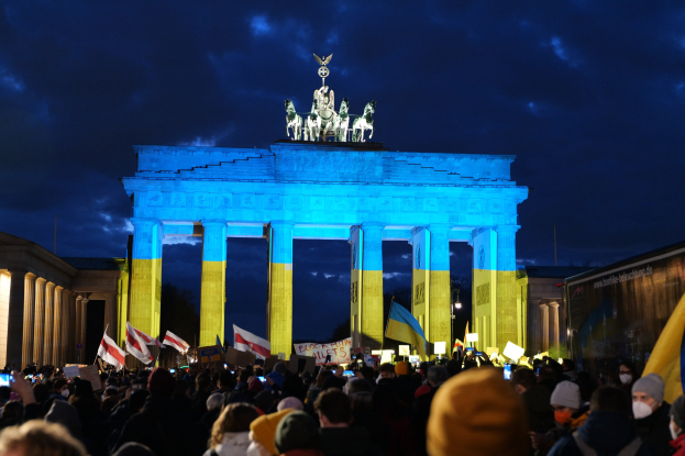 Eine Menschenmenge steht vor dem Brandenburger Tor in Berlin, Deutschland, mit Fahnen und Schildern, mit einer Fahne auf der rechten Seite.