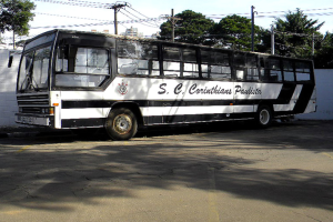Ein Bus parkt auf einer Straße mit einer Wand, Strommasten mit Kabeln, Bäumen, Gebäuden und dem Himmel im Hintergrund.