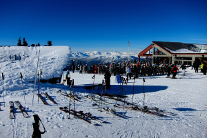 Eine Gruppe von Menschen auf einer verschneiten Landschaft mit Gebäuden, Skiern, einer Flagge und Polen, mit einem Berg und Himmel im Hintergrund.