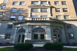 Großes Glasgebäude der University Tower Apartments in Chicago, Illinois, mit umgebender Vegetation und einem Schild davor.