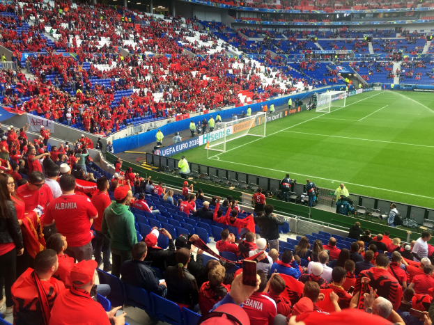 Ein volles Stadion mit Zuschauern, Fahnen und einem sichtbaren Torpfosten unter einer Decke mit Deckenleuchten, während Fans gespannt auf ein Fußballspiel warten.