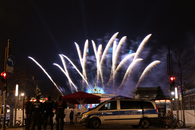 Polizeifahrzeug vor Menschenmenge unter bunten Feuerwerken und Gebäudelichtern geparkt.