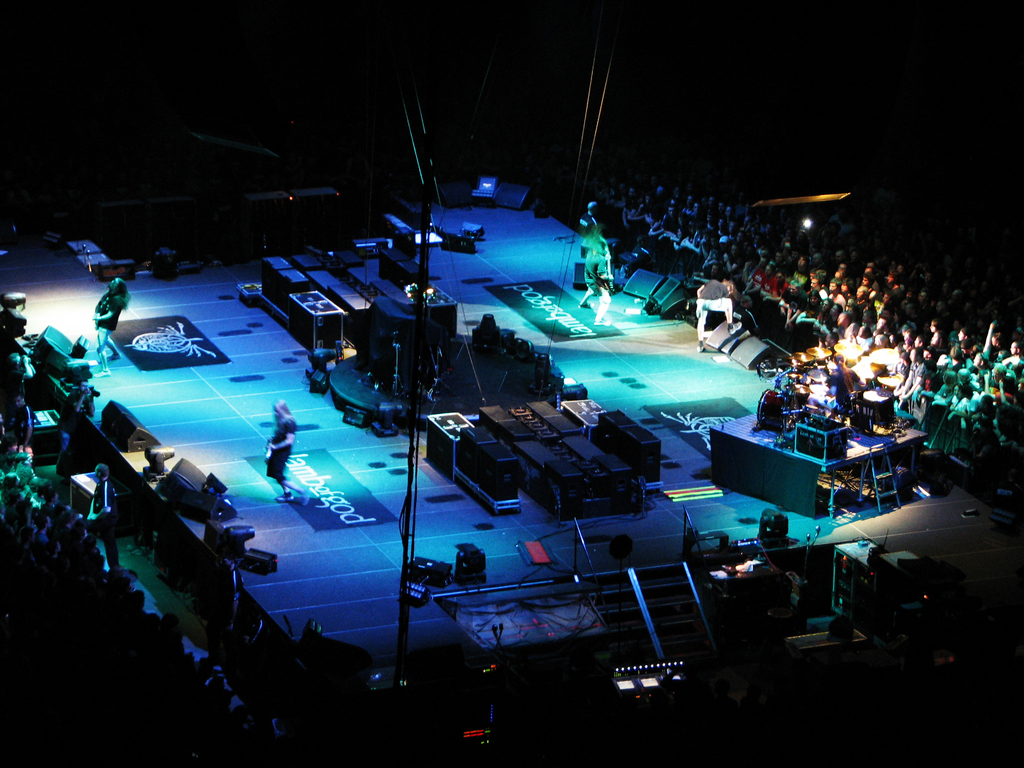 Eine Bühne mit Performern, Equipment und einer großen Zuschauermenge auf beiden Seiten in einem dunklen Hintergrund.