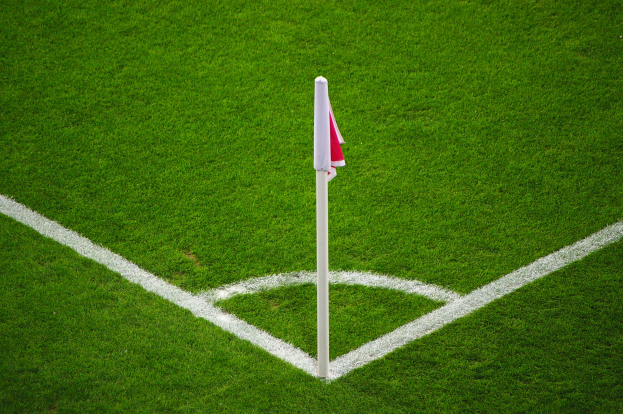 Ein Fußballfeld mit grünem Gras, weißen Begrenzungslinien und einem weißen Pfosten mit einer roten und weißen Flagge am zentralen Strafpunkt.