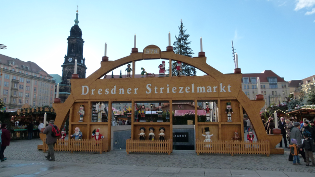 Ein geschäftiger Weihnachtsmarkt in Dresden, Deutschland mit Menschen, die spazieren gehen, einem Bogen, Bäumen, Gebäuden und einem bewölkten Himmel.