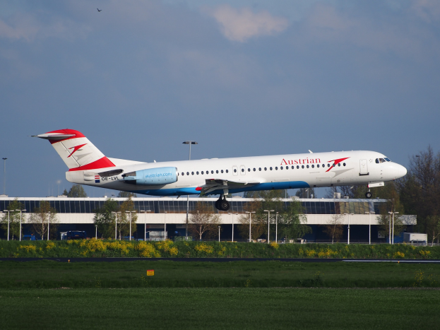 Ein Austrian-Airlines-Airbus-A320-200 beim Starten am Frankfurter Flughafen mit Grünflächen, Laternen, einem Gebäude und einer bewölkten Himmel im Hintergrund.