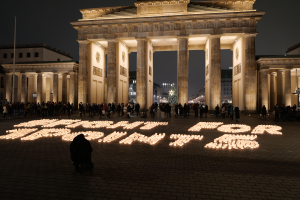 Eine Gruppe von Menschen, die vor dem beleuchteten Brandenburger Tor in Berlin, Deutschland, mit den Worten 'Kämpfe für die Freiheit' im Vordergrund stehen.