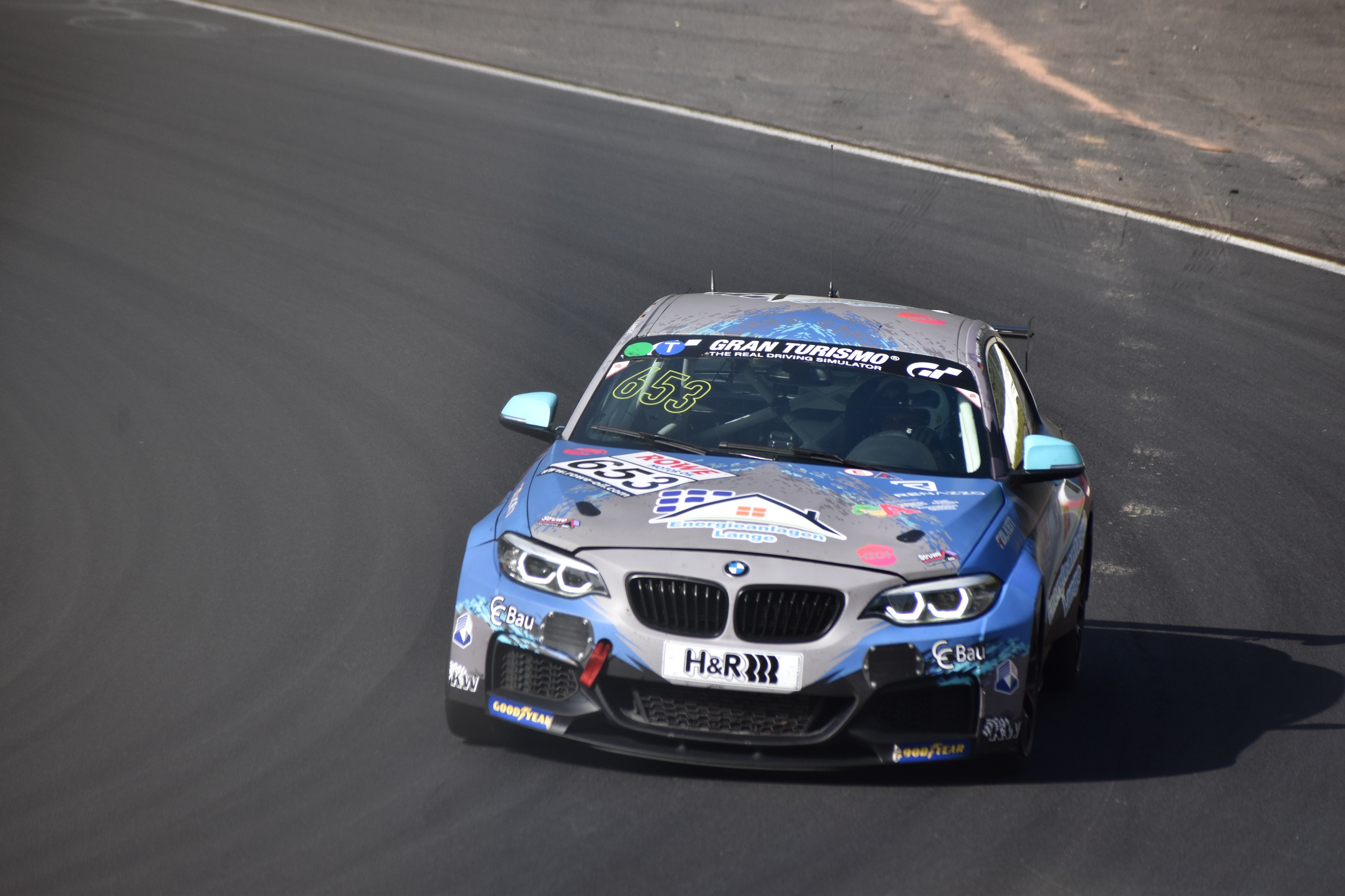 BMW M2 GT3 Rennwagen auf einer Rennstrecke mit Text und Zahlen auf der Karosserie.