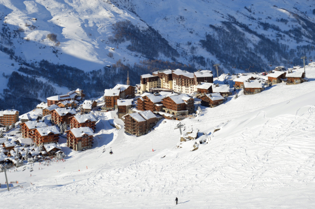 Ein malerischer Blick auf ein Skigebiet in den französischen Alpen mit schneebedeckten Bergen, Gebäuden, Bäumen und Skifahrern auf den Pisten.