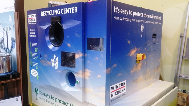 Blaues Recyclingzentrum mit einem "Recyclingzentrum"-Schild in der Mitte, einem Ständer mit verschiedenen Gegenständen links daneben, einem einzelnen Gegenstand auf dem Boden rechts daneben und Hintergrundbeleuchtung und Wand.