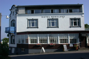 Das Hotel Nordland in Stavanger, Norwegen, ein mehrstöckiges Gebäude mit zahlreichen Fenstern, einem Schild mit Text, einem Straßenpfosten, einer Gruppe von Bäumen davor und einem bewölkten Himmel im Hintergrund.