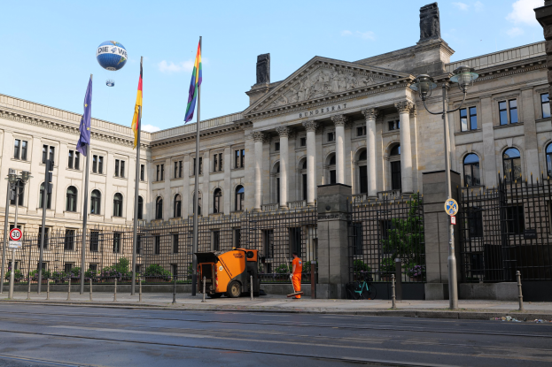 Großes modernes Gebäude mit zahlreichen Fenstern, als Bundestag in Berlin, Deutschland identifiziert, umgeben von Straßeninfrastruktur, Fahrzeugen, Fußgängern und Bäumen unter einem bewölkten Himmel.